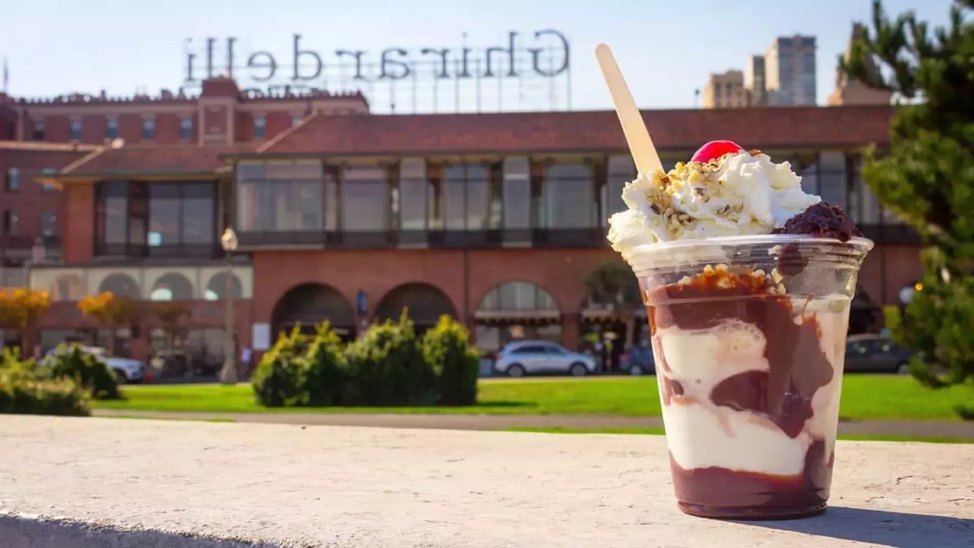 A chocolate sundae sits in the foreground with Ghirardelli Square in the background.