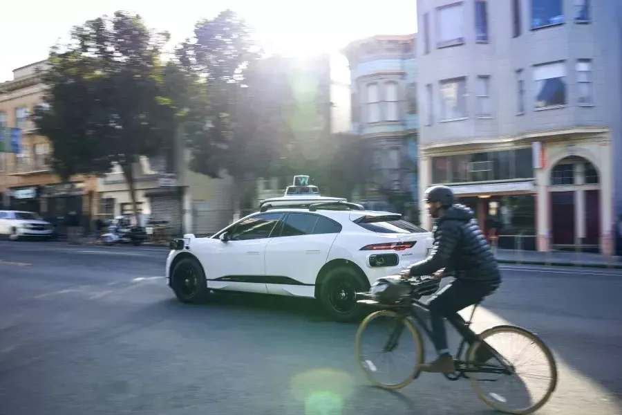 Pessoa andando de bicicleta atrás de um carro Waymo